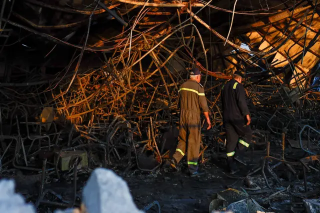 Officials walk through the rubble at the site following a fatal fire at a wedding celebration