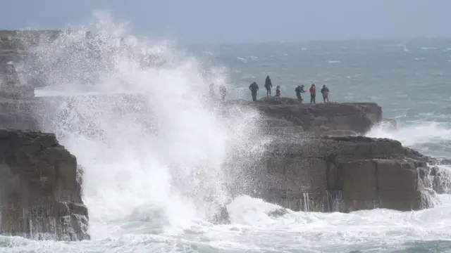 People watch as waves crash against the shore in Portland, Dorset