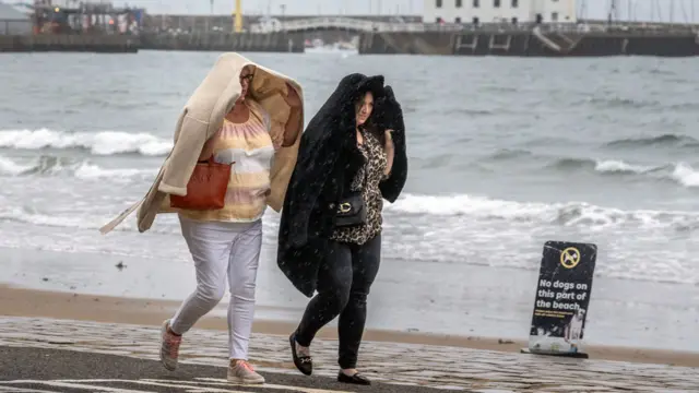 Two women walk along the sea front in Scarborough, North Yorkshire, covering their heads with their cardigans