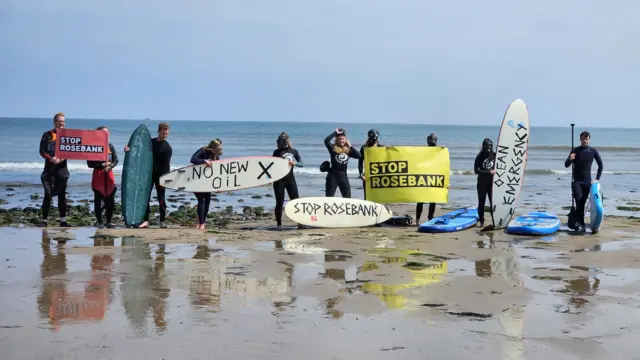 Members of the group Surfers Against Sewage are seen on a beach in Aberdeen protesting the Rosebank oil field, holding up signs and surfboards sporting anti-oil messages