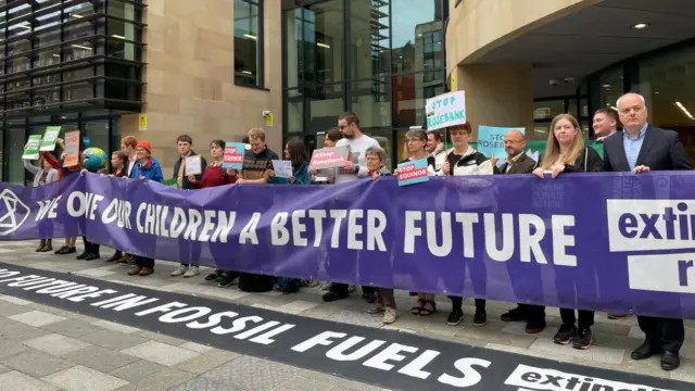 Protesters outside a UK government building in Edinburgh hold up signs with slogans against Rosebank