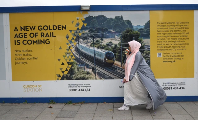 A woman walks past advertising hoarding for the HS2 High speed rail link by the Cursor Station terminus in Birmingham