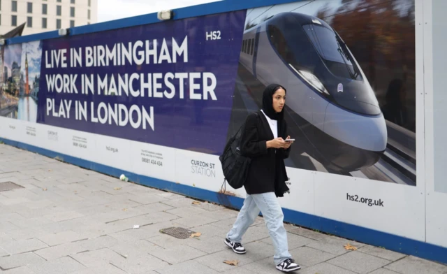 A woman walks past advertising hoarding for the HS2 High speed rail link by the Cursor Station terminus in Birmingham