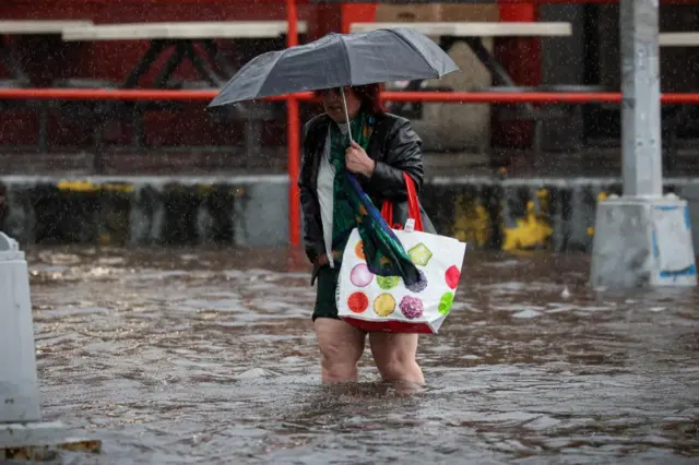 A woman walks through rain and flood waters