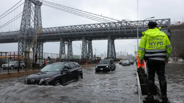 A police officer from the NYPD Highway Patrol looks to motorists drive through a flooded street