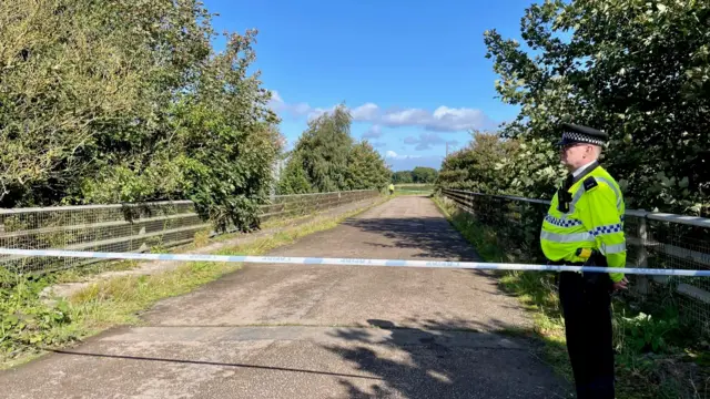 A police officer guards a cordon across a bridge overlooking the M53 motorway