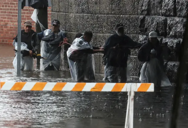 People in Westchester County grip a wall as they try to walk through flood water