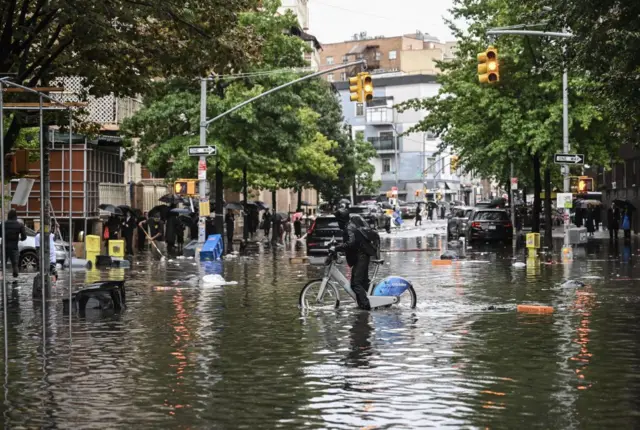 A man tries to pass a flooded street with his bicycle after a heavy rain in Williamsburg, New York