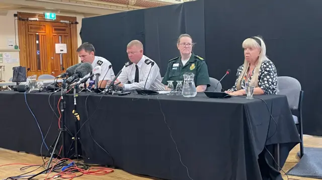 Simone White speaks beside colleagues at a black table with microphones