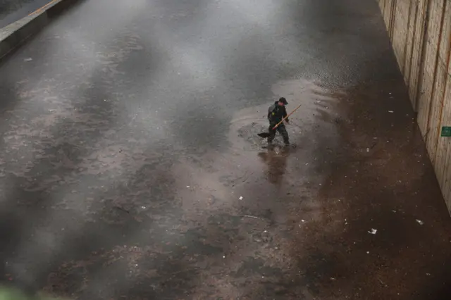 A person tries to unclog a drain on the flooded Prospect Expressway