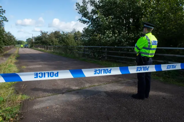 A police officer stands in front of police tape blocking off a bridge on the M53