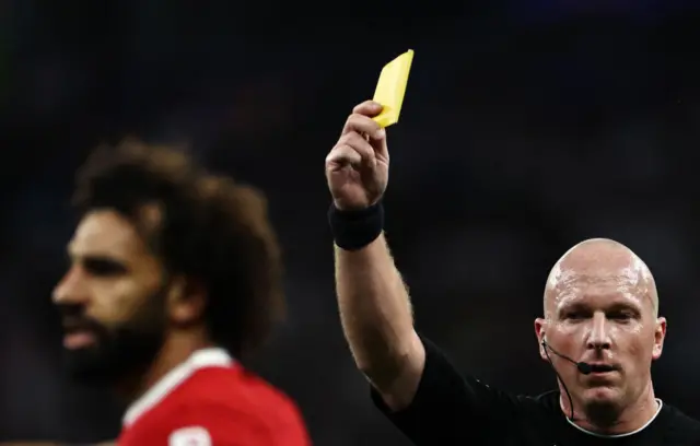 Referee Simon Hooper gives a yellow card to Mohamed Salah