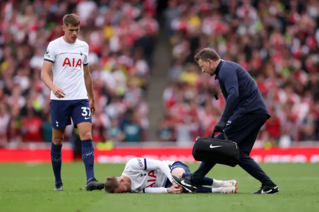 James Maddison holds his knee while lying on the floor as a physio runs onto the field.