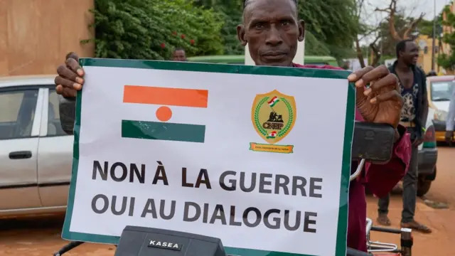 A supporter of the military junta displays a sign that reads 'No to war, yes, to dialogue' during a protest against a potential military intervention in Niamey, Niger, 20 August 2023