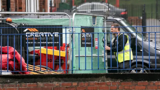 A construction worker handles pop-up fencing at a school