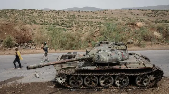 Local farmers walk next to a tank of alledged Eritrean army that is abandoned along the road in Dansa, southwest of Mekele in Tigray region, Ethiopia, on June 20, 2021.