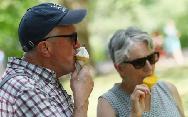 A couple eat ice-cream and lollies in St James' Park in London in June 2023