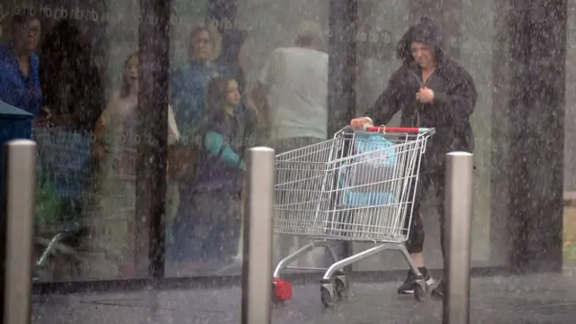 A woman in a black raincoat with an empty shopping trolley is caught in a heavy downpour in Liverpool