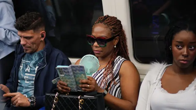 A commuter with a portable handheld fan on a Jubilee line train