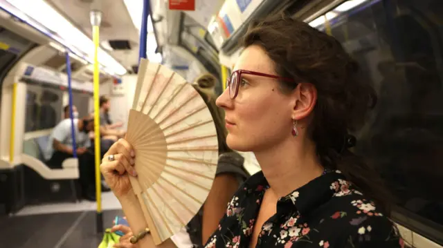 A woman uses a fan to cool herself in a train on the London Underground