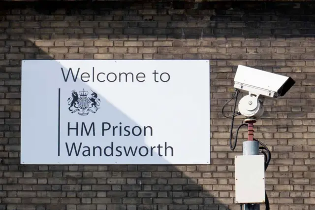 A sign that reads 'welcome to hm prison wandsworth' and a cctv camera outside the penitentiary