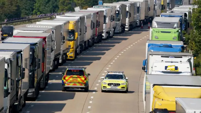 Police cars patrol a queue of lorries on a motorway