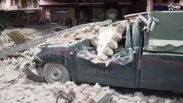 A car is seen crushed and covered in debris in Marrakesh