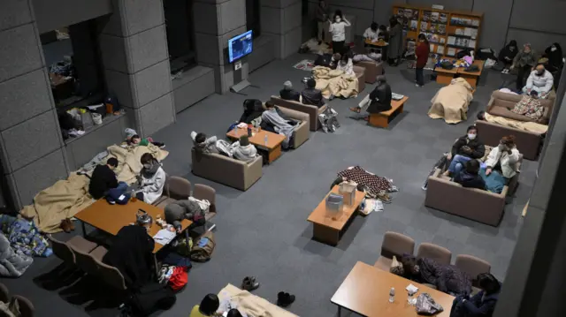 Evacuees sit and rest on sofas and at tables in government office in Kanazawa