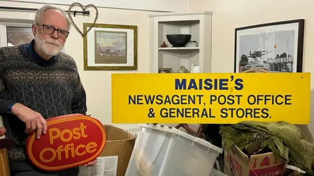 John Hanna holding a Post Office sign inside