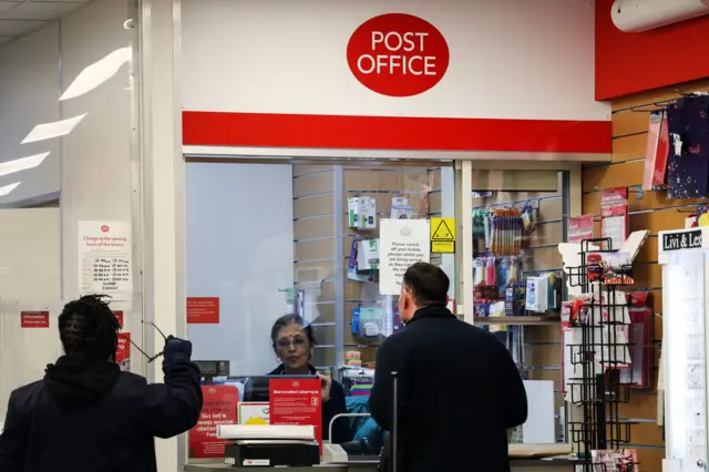 An employee assists people at a post office in the UK