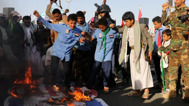 Crowds gather around burning Israeli and American flags