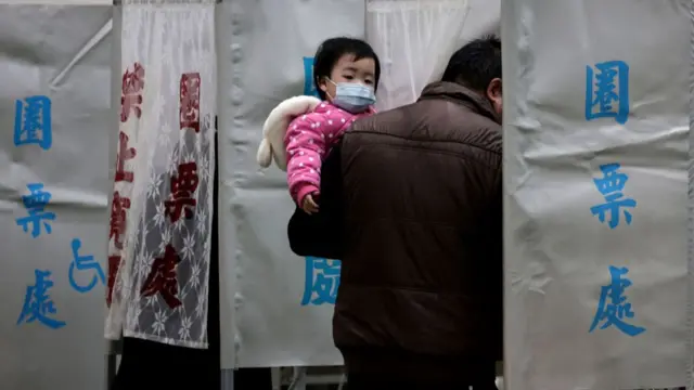 A man carries a child as he casts his ballot to vote in the presidential election at a polling station in a high school in Tainan