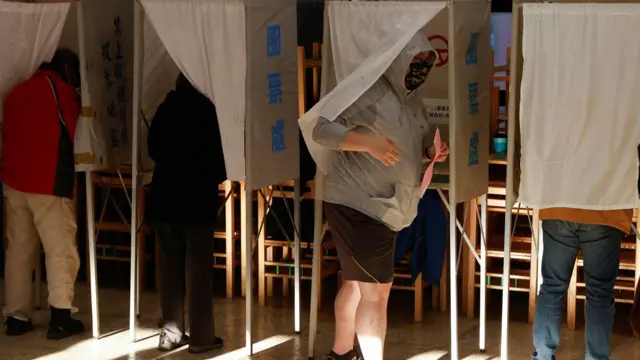 A man walks out from a voting booth before casting his ballot during the presidential and parliamentary elections in Taipei