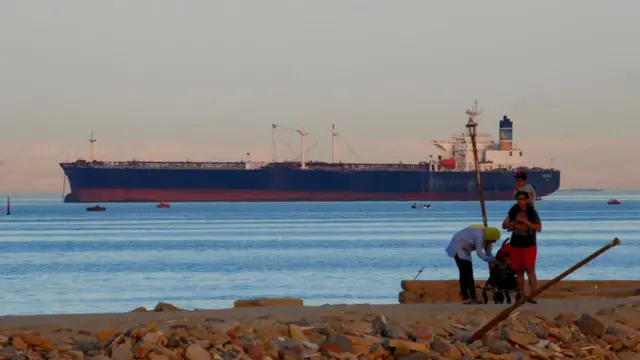 People walk on the beach as a container ship crosses the Gulf of Suez towards the Red Sea