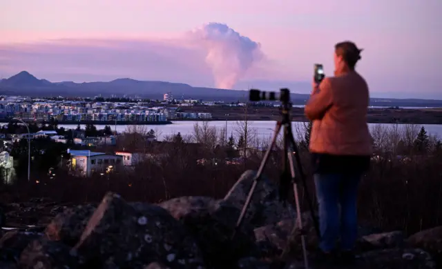 A woman takes pictures of the volcanic eruption from Rejkyavik