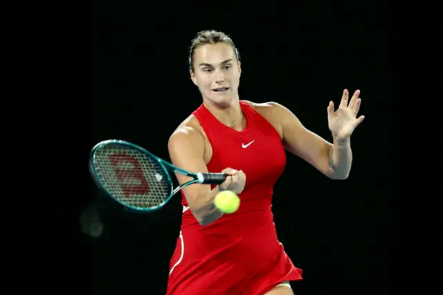 Aryna Sabalenka hits a forehand shot in her red Nike dress.