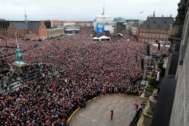 The crowd watch the King [on the right hand side of the frame] on parliament's balcony