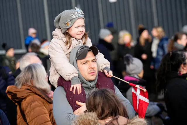 A girl holding a Danish flag sits on a man's shoulders