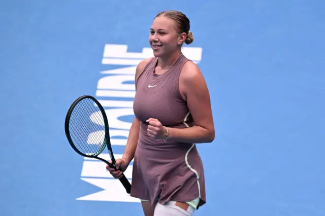 Amanda Anisimova clenches her fist and smiles in celebration wearing a pink Nike dress with strapping on her left thigh.