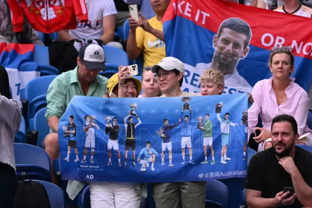 Fans of Novak Djokovic hold banners in support in the crowd.