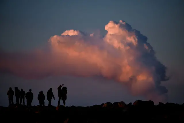 People watch the billowing smoke during a volcanic eruption north of the south-western Icelandic town of Grindavik