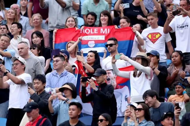 Fans of Novak Djokovic hold banners in support in the crowd.