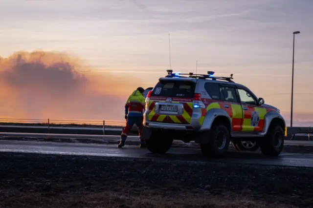 An emergency vehicle with smoke from the volcanic eruption which can be seen in the distance