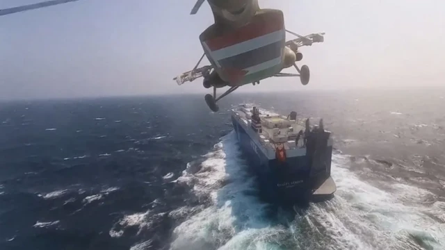 A Houthi military helicopter flies over a large ship in the Red Sea