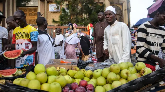 A street vendor sells watermelons/apple as he waits for customers at the entrance of the Lagos Central Mosque