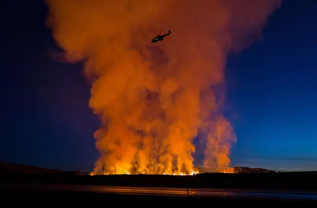 A helicopter flies near smoke rising as a volcano erupts in Grindavik