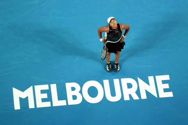 Naomi Osaka looks up as she stands next to the Melbourne sign on Rod Laver Arena