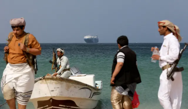 Armed men stand on the beach as the Galaxy Leader commercial ship, seized by Houthis last year, is anchored off the coast of al-Salif, Yemen