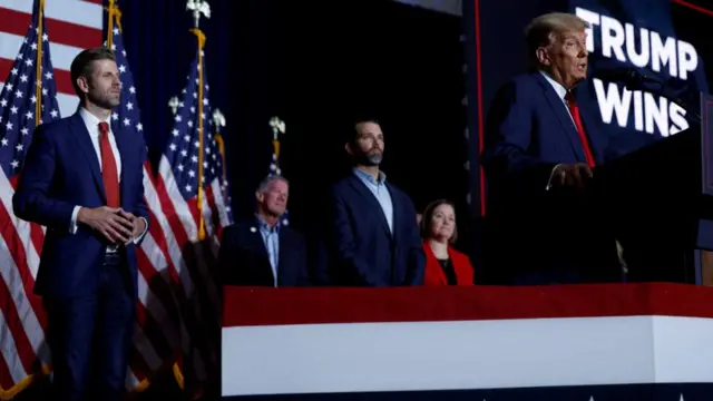 Trump speaks at a lectern - behind him a screen reads "Trump wins"