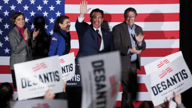 DeSantis grins and waves at a crowd holding up signs bearing his name